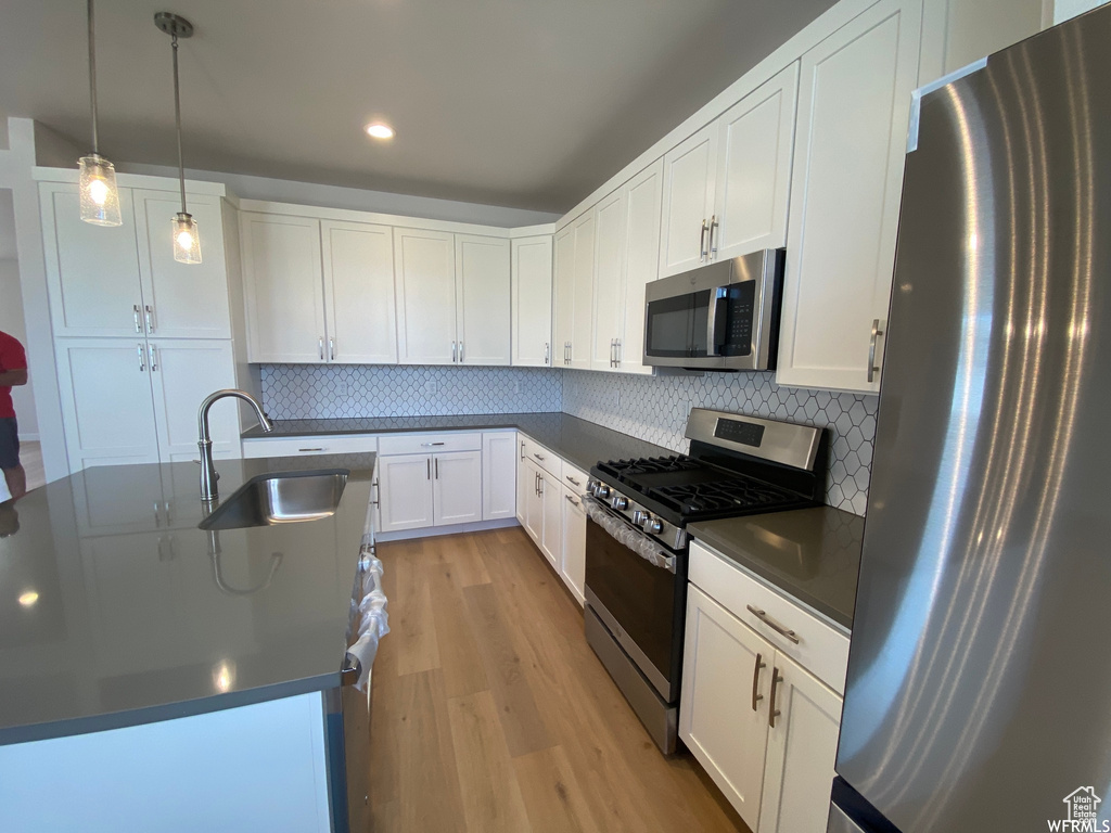 Kitchen with pendant lighting, stainless steel appliances, tasteful backsplash, light hardwood / wood-style flooring, and sink