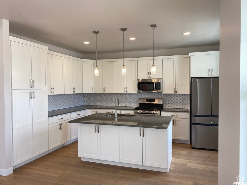 Kitchen featuring stainless steel appliances, white cabinets, pendant lighting, and light hardwood / wood-style floors