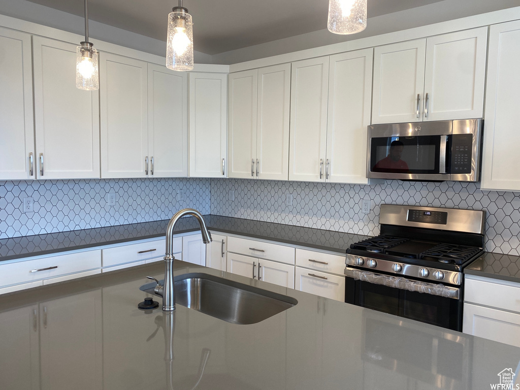 Kitchen featuring appliances with stainless steel finishes, white cabinetry, backsplash, and decorative light fixtures