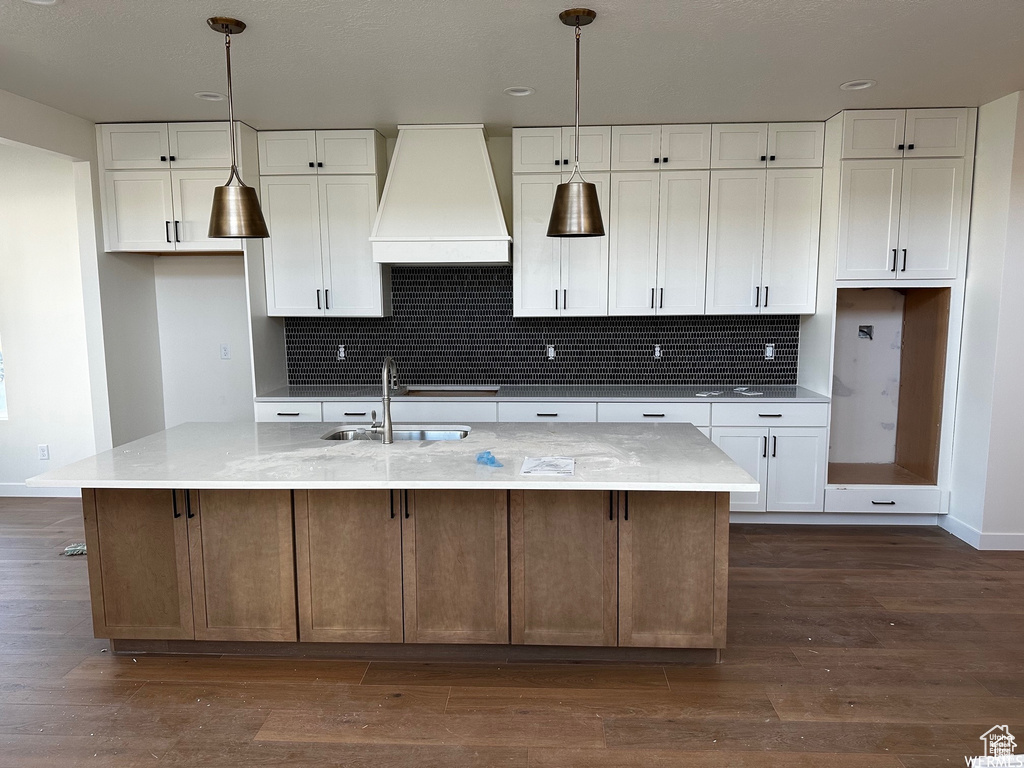 Kitchen featuring white cabinets, a kitchen island with sink, premium range hood, and dark wood-type flooring
