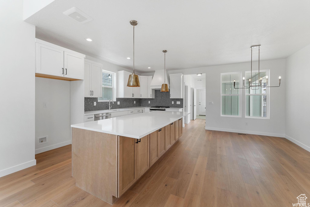Kitchen with pendant lighting, a notable chandelier, white cabinetry, a kitchen island, and light hardwood / wood-style floors