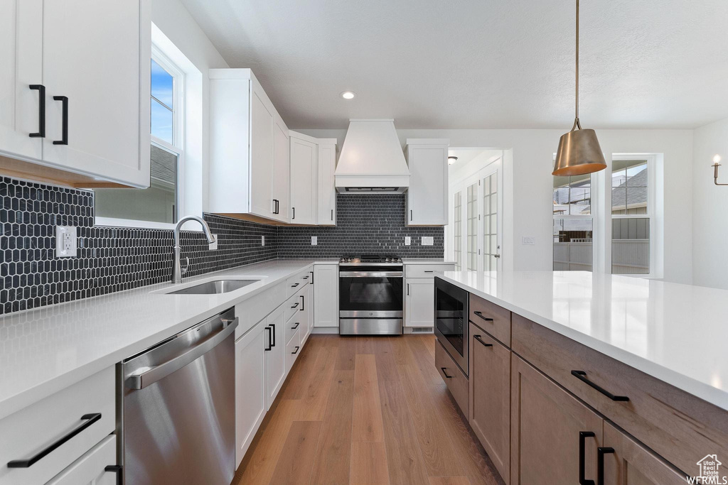 Kitchen with white cabinets, appliances with stainless steel finishes, pendant lighting, and light wood-type flooring