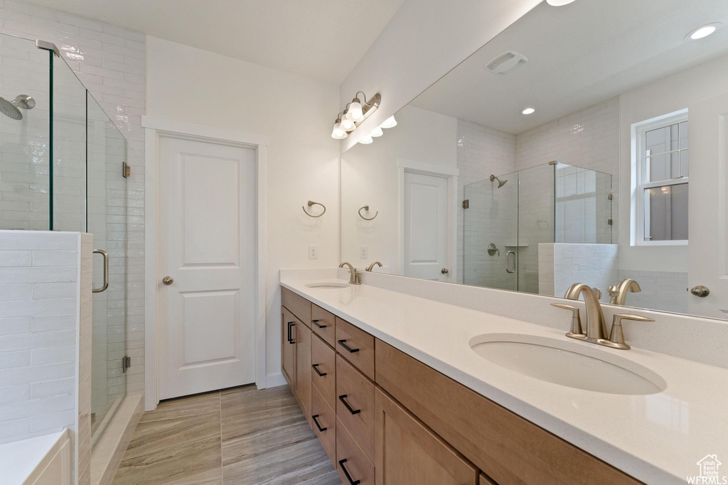 Bathroom with vanity with extensive cabinet space, double sink, and a shower with door
