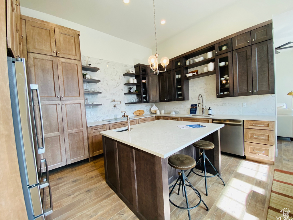 Kitchen featuring light hardwood / wood-style flooring, backsplash, an island with sink, a notable chandelier, and stainless steel appliances