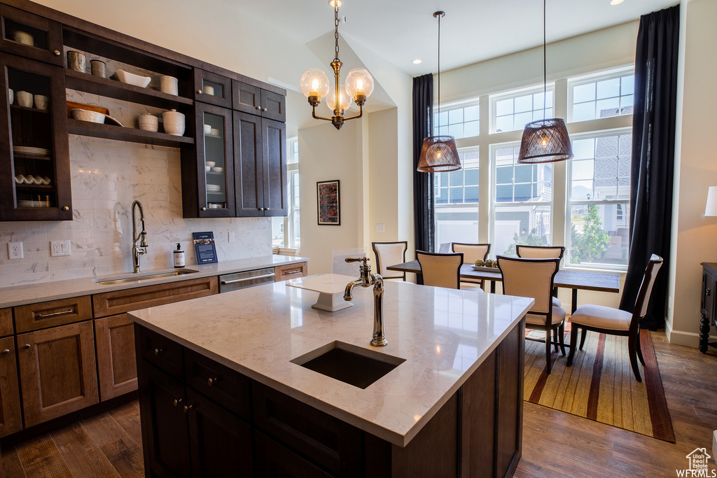 Kitchen with dark hardwood / wood-style flooring, an inviting chandelier, a kitchen island with sink, and sink
