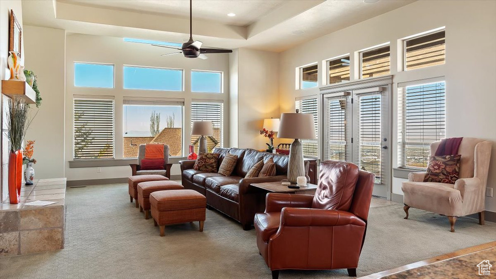 Living room featuring a towering ceiling, french doors, light colored carpet, ceiling fan, and a tray ceiling