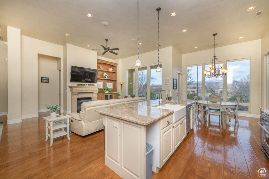 Kitchen featuring ceiling fan with notable chandelier, light stone counters, white cabinetry, light hardwood / wood-style floors, and a kitchen island with sink