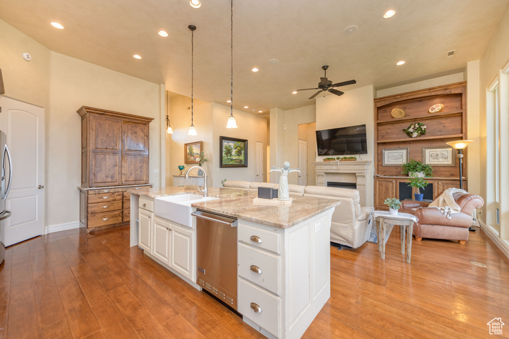 Kitchen featuring dishwasher, light wood-type flooring, white cabinets, ceiling fan, and an island with sink