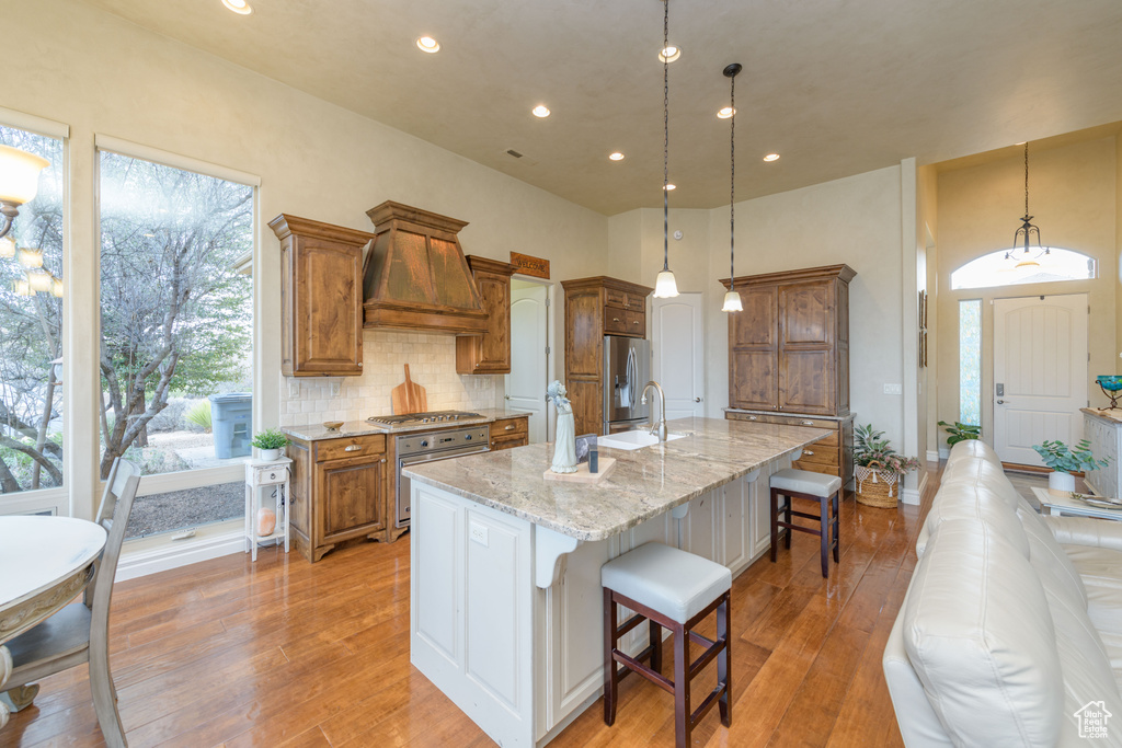 Kitchen featuring a center island with sink, light stone countertops, light hardwood / wood-style floors, and a kitchen bar