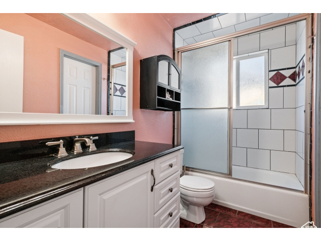 Full bathroom featuring enclosed tub / shower combo, vanity, tile flooring, and toilet