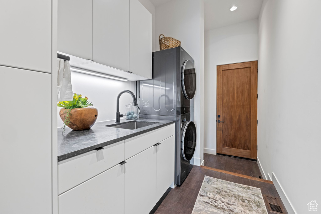 Washroom featuring estacked washer and dryer, cabinet space, dark wood-style floors, baseboards, and recessed lighting