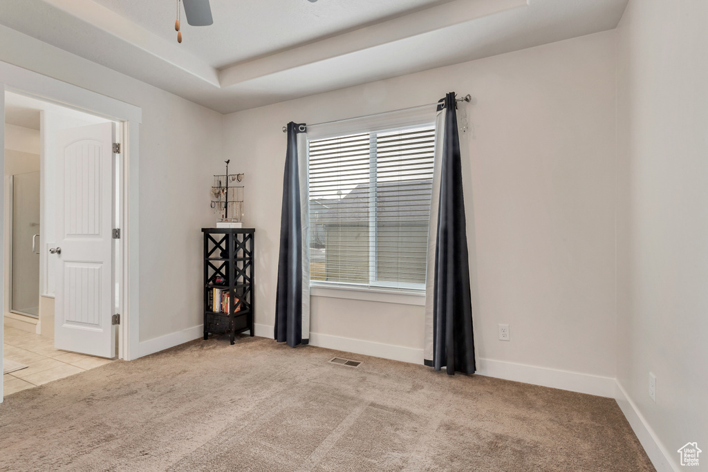 Carpeted spare room featuring a tray ceiling and ceiling fan