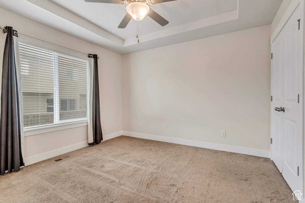 Empty room featuring light colored carpet, ceiling fan, and a raised ceiling