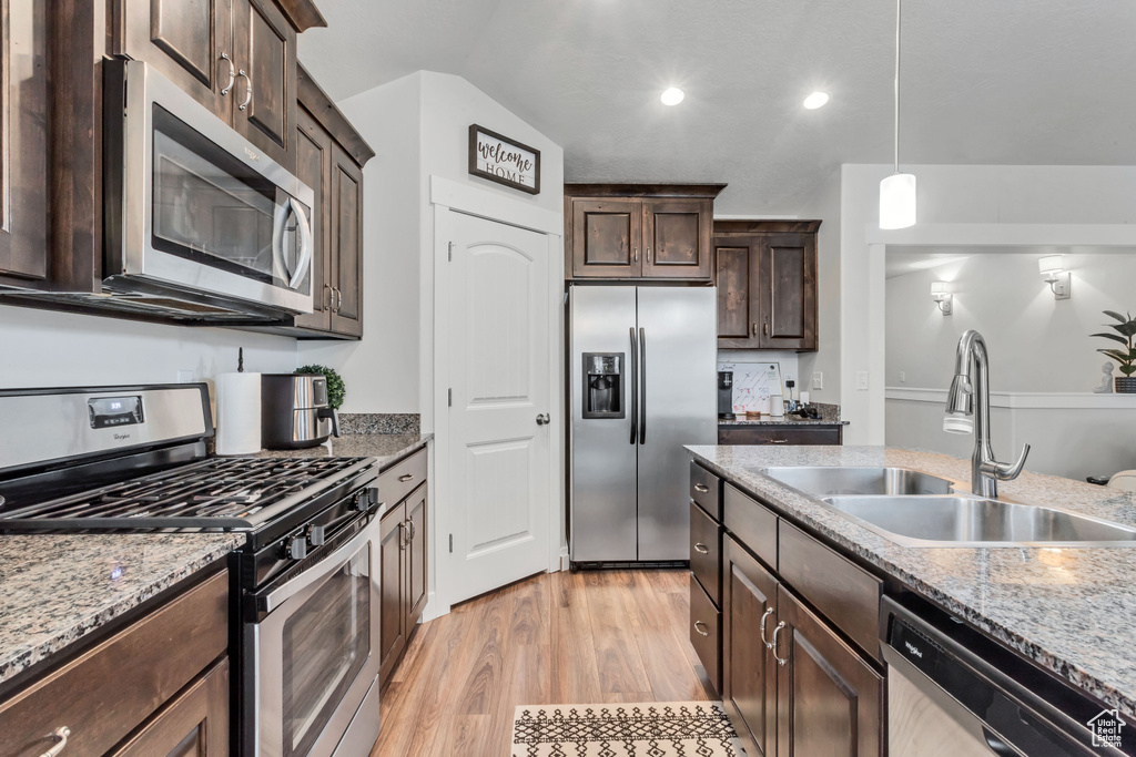 Kitchen with pendant lighting, stainless steel appliances, light stone counters, light hardwood / wood-style flooring, and sink