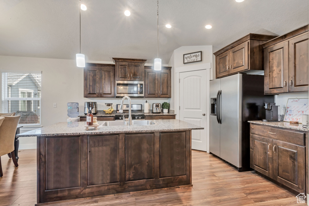 Kitchen featuring pendant lighting, dark brown cabinetry, lofted ceiling, appliances with stainless steel finishes, and light hardwood / wood-style flooring