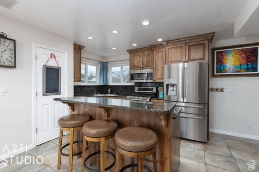Kitchen with a kitchen breakfast bar, light tile floors, dark stone countertops, appliances with stainless steel finishes, and a center island