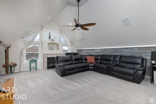 Carpeted living room with lofted ceiling, ceiling fan, and a tiled fireplace