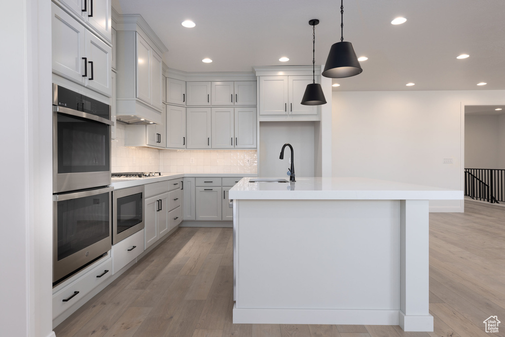 Kitchen featuring sink, white cabinets, light hardwood / wood-style floors, backsplash, and a center island with sink