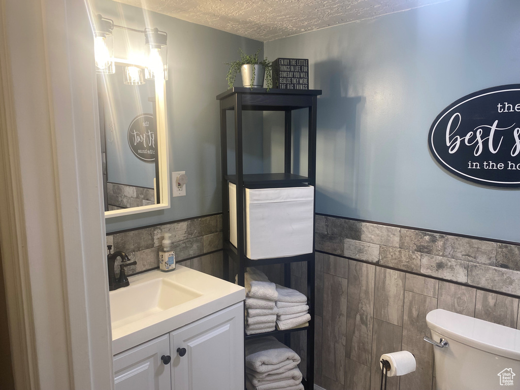 Bathroom featuring tasteful backsplash, a textured ceiling, tile walls, toilet, and vanity