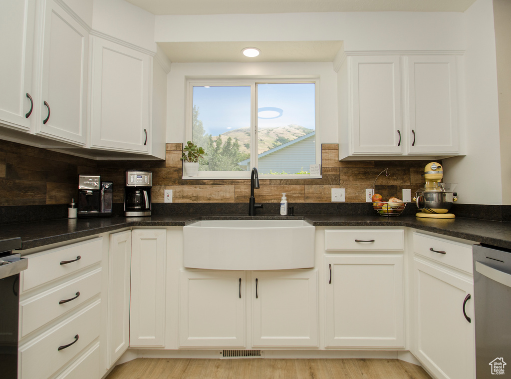 Kitchen featuring sink, tasteful backsplash, light hardwood / wood-style floors, and white cabinets