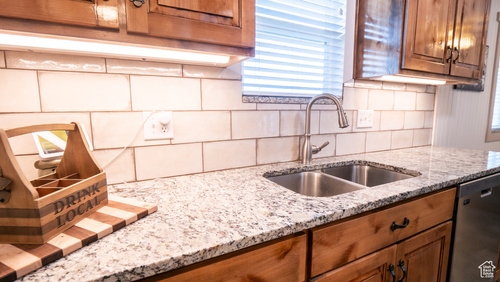 Kitchen featuring sink, backsplash, light stone counters, and stainless steel dishwasher