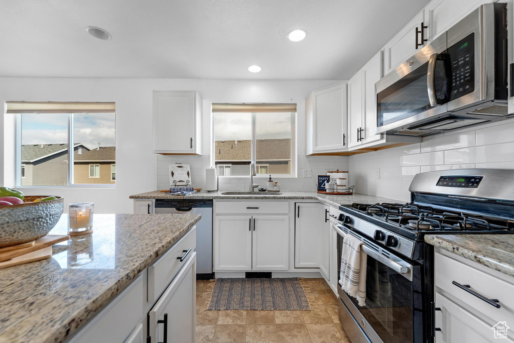 Kitchen with a wealth of natural light, appliances with stainless steel finishes, tasteful backsplash, and white cabinets