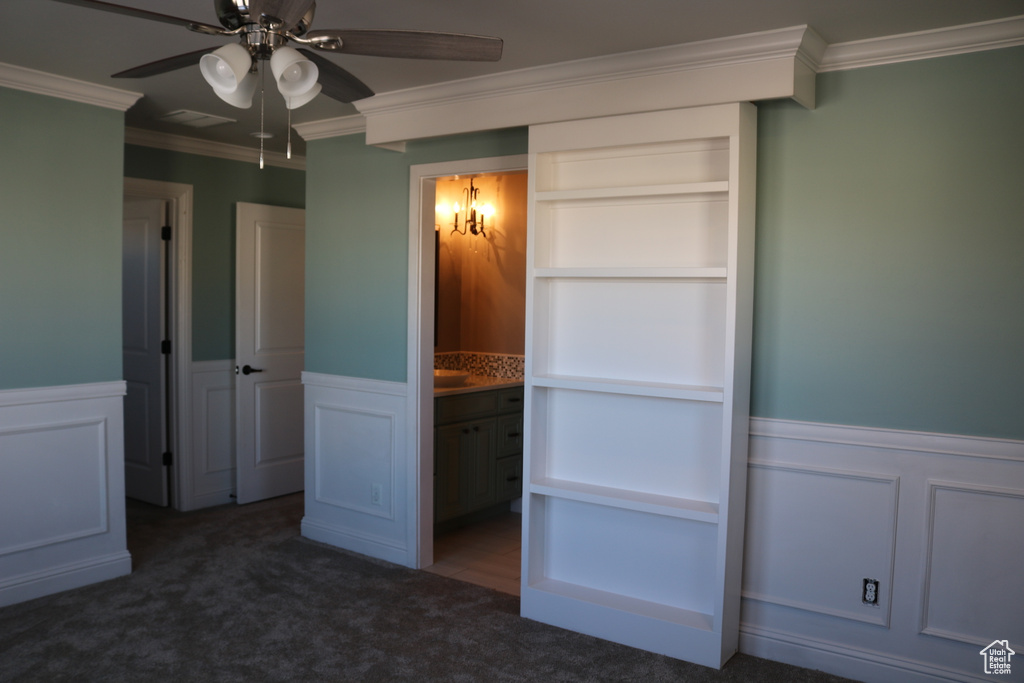 Unfurnished bedroom featuring ornamental molding, dark carpet, a closet, connected bathroom, and ceiling fan