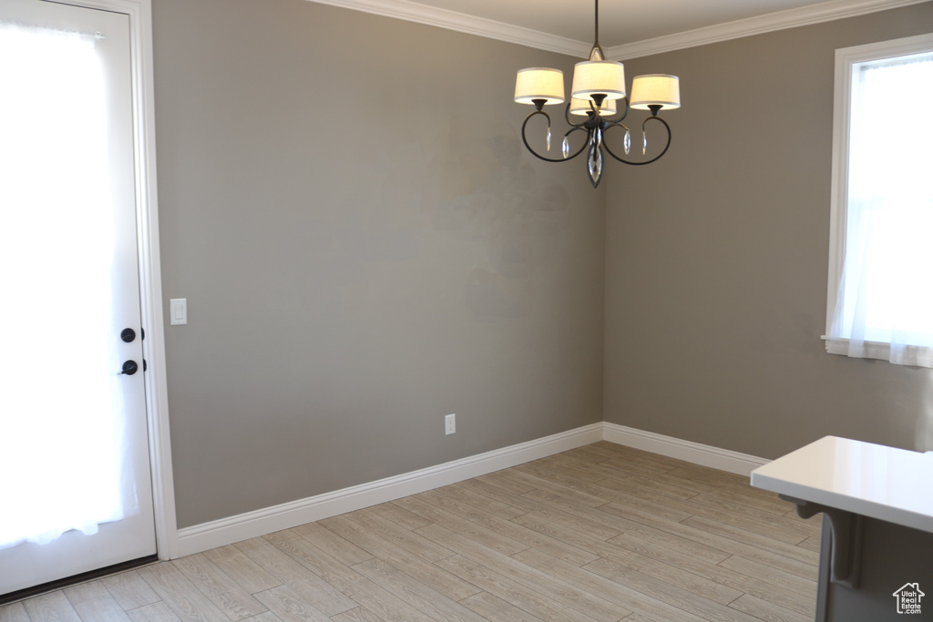 Empty room with an inviting chandelier, crown molding, and light wood-type flooring