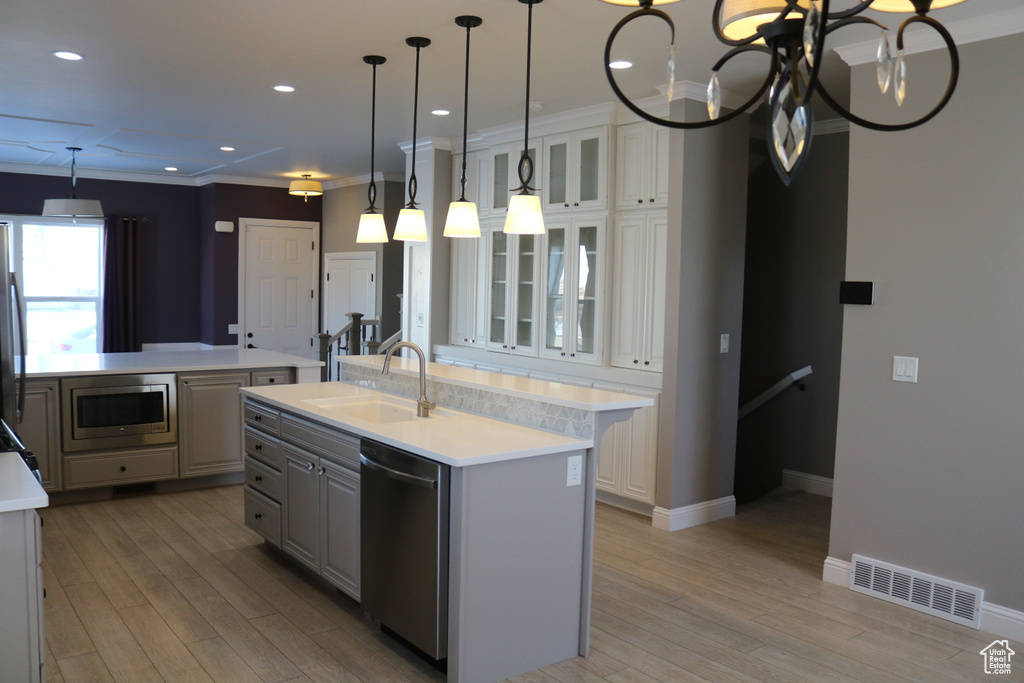 Kitchen with hanging light fixtures, appliances with stainless steel finishes, light hardwood / wood-style flooring, an island with sink, and sink