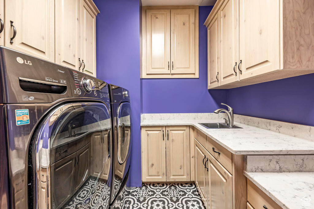 Laundry room featuring washing machine and clothes dryer, light tile floors, cabinets, and sink