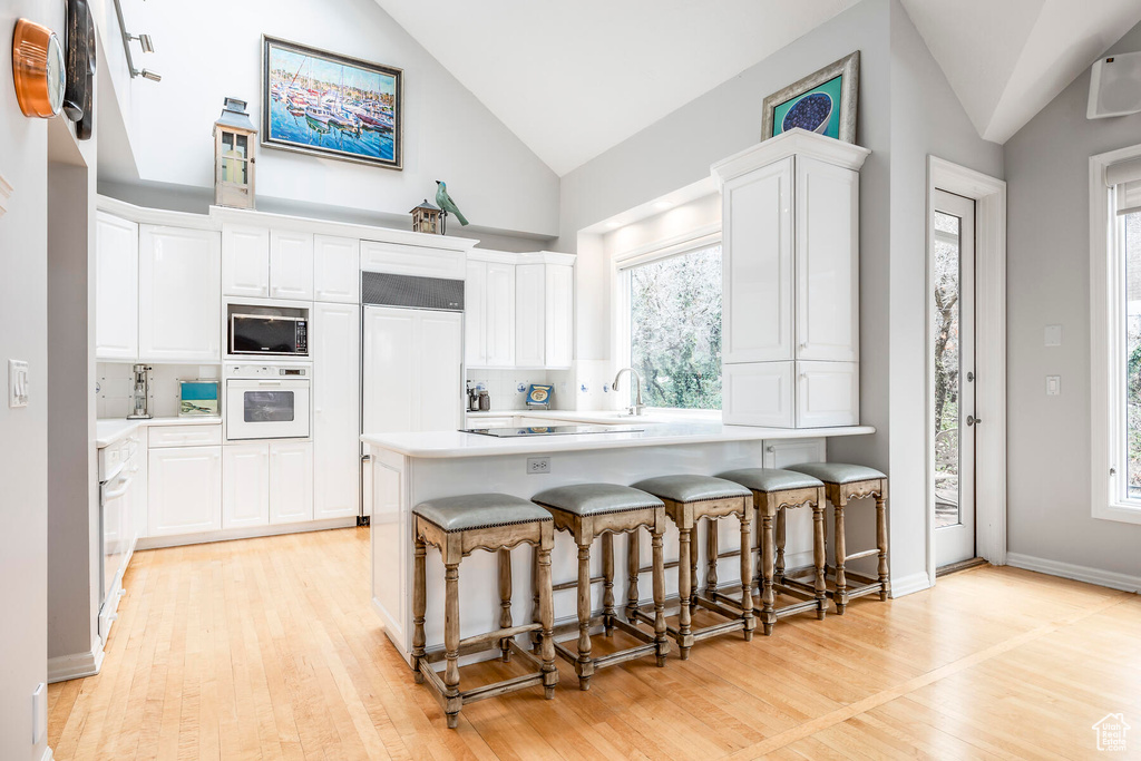 Kitchen featuring white cabinetry, light hardwood / wood-style floors, a kitchen bar, and built in appliances