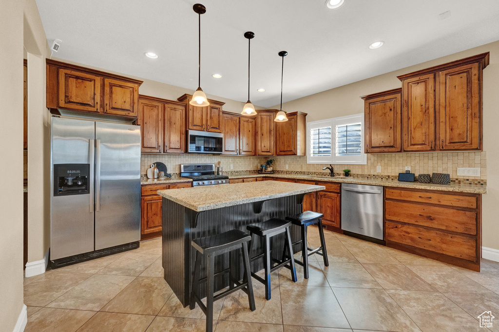 Kitchen featuring a kitchen island, tasteful backsplash, appliances with stainless steel finishes, a kitchen breakfast bar, and decorative light fixtures