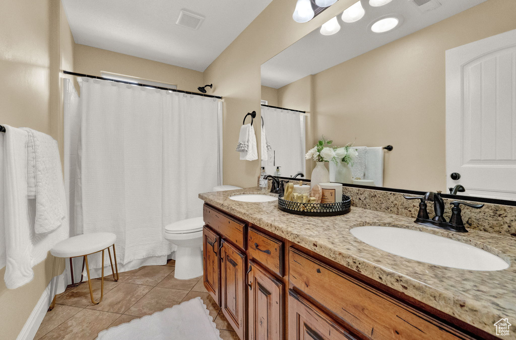 Bathroom featuring double sink vanity, tile flooring, and toilet