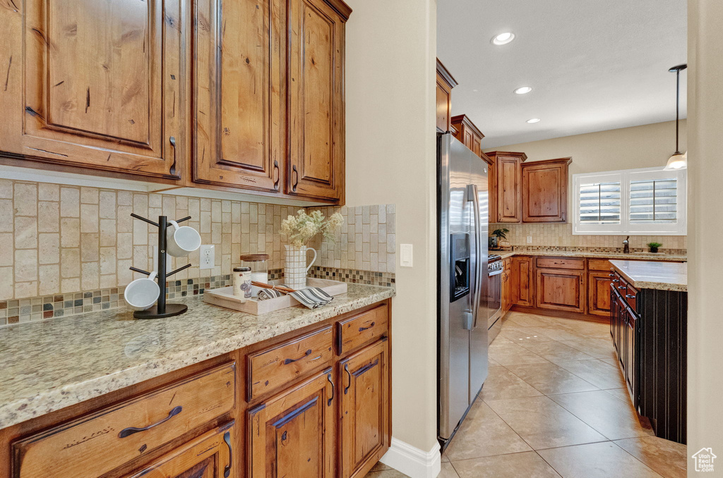 Kitchen with light tile flooring, light stone counters, backsplash, and stainless steel fridge