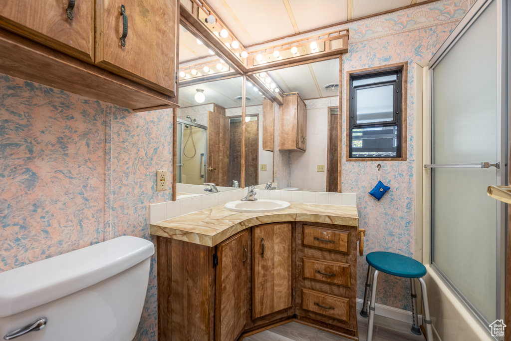 Full bathroom with bath / shower combo with glass door, large vanity, toilet, and wood-type flooring