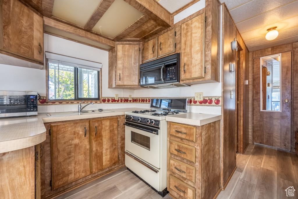 Kitchen featuring white gas stove, sink, wooden walls, and light hardwood / wood-style floors