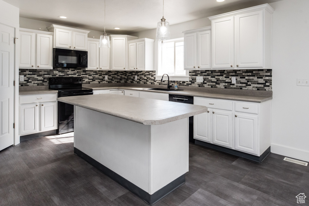 Kitchen with hanging light fixtures, white cabinets, black appliances, and a kitchen island