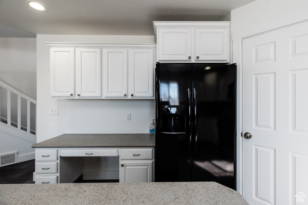 Kitchen with black refrigerator with ice dispenser, light stone countertops, and white cabinets