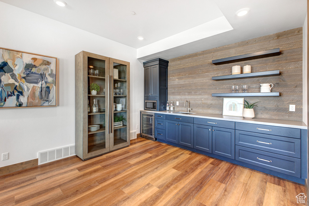 Bar with blue cabinetry, tasteful backsplash, light hardwood / wood-style floors, beverage cooler, and sink