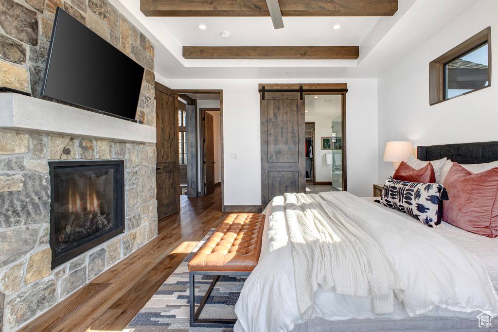 Bedroom with a fireplace, a barn door, dark wood-type flooring, and a raised ceiling