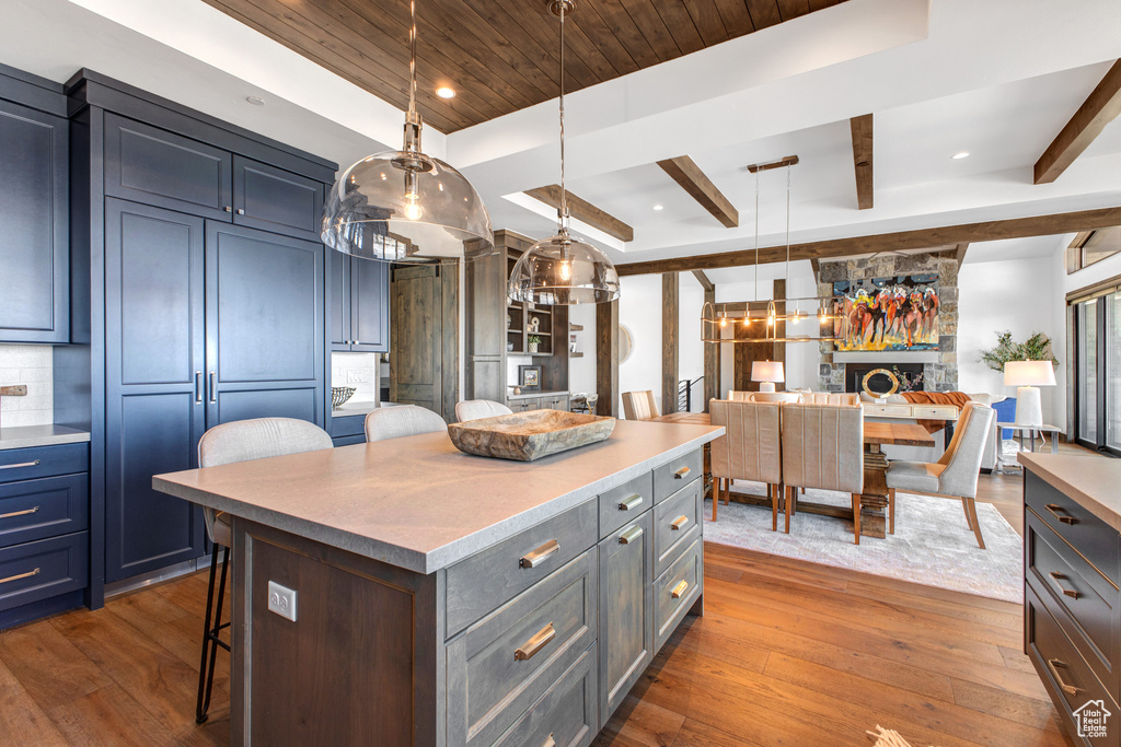 Kitchen featuring a breakfast bar, beamed ceiling, hanging light fixtures, a center island, and dark wood-type flooring