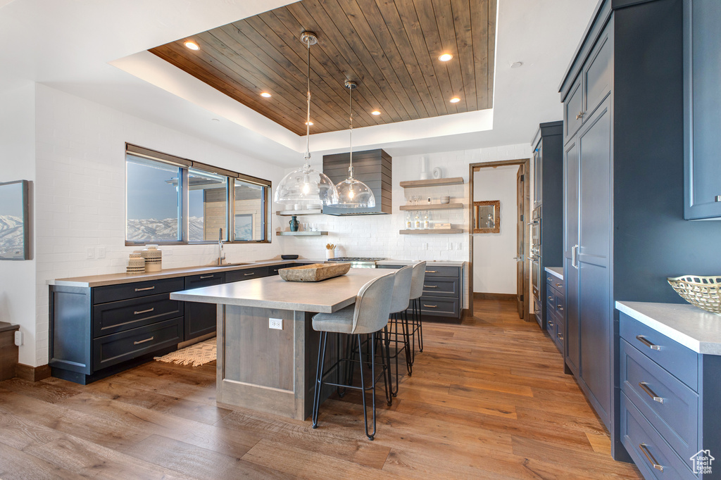 Kitchen featuring a kitchen island, a tray ceiling, light wood-type flooring, and a kitchen breakfast bar