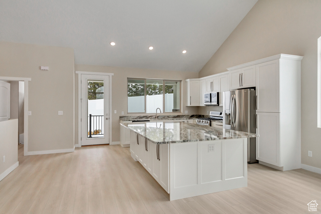 Kitchen with light stone countertops, a kitchen island, white cabinetry, and light hardwood / wood-style floors