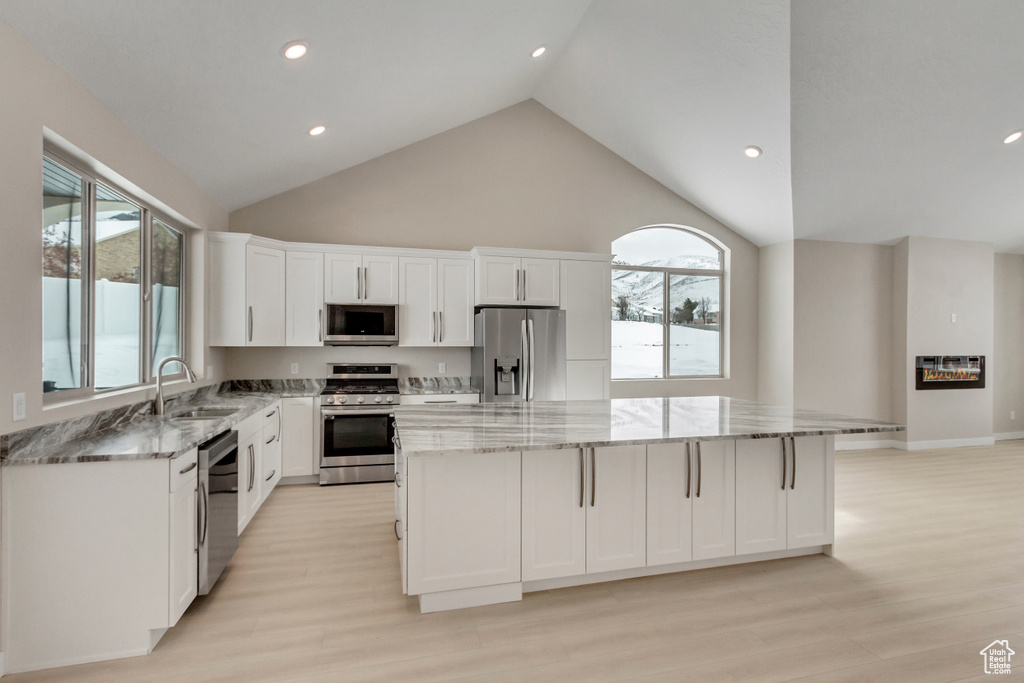 Kitchen with stainless steel appliances, white cabinets, a kitchen island, and light hardwood / wood-style flooring