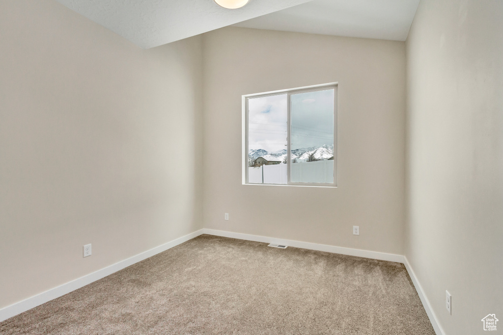 Empty room featuring light carpet and vaulted ceiling