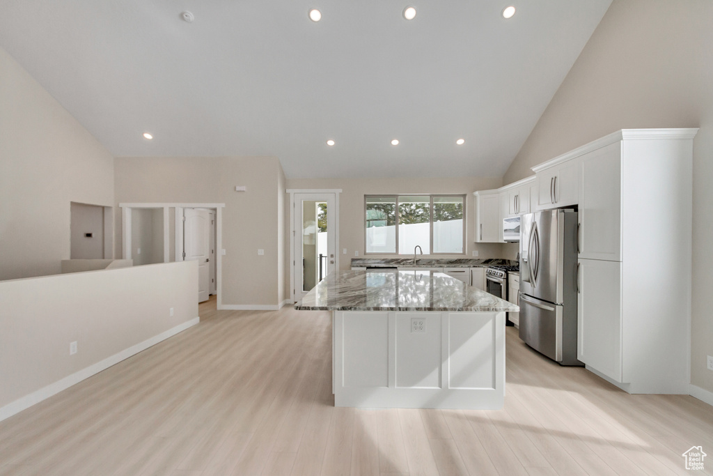 Kitchen with light hardwood / wood-style floors, a kitchen island, light stone countertops, stainless steel appliances, and high vaulted ceiling