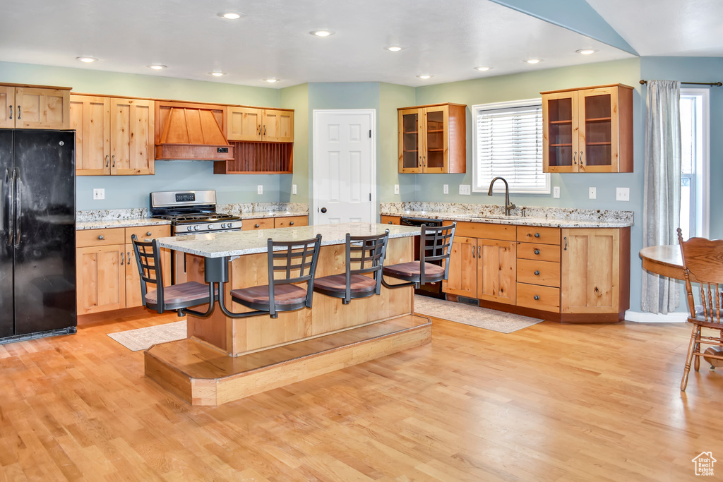 Kitchen featuring light hardwood / wood-style flooring, light stone countertops, custom range hood, black fridge, and stainless steel gas stove