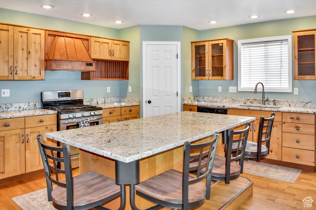 Kitchen with light stone countertops, light hardwood / wood-style floors, gas stove, custom range hood, and sink