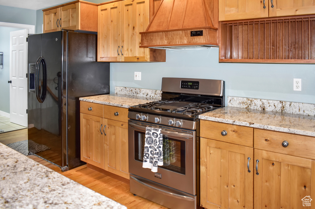 Kitchen featuring premium range hood, light wood-type flooring, light stone counters, gas range, and black fridge