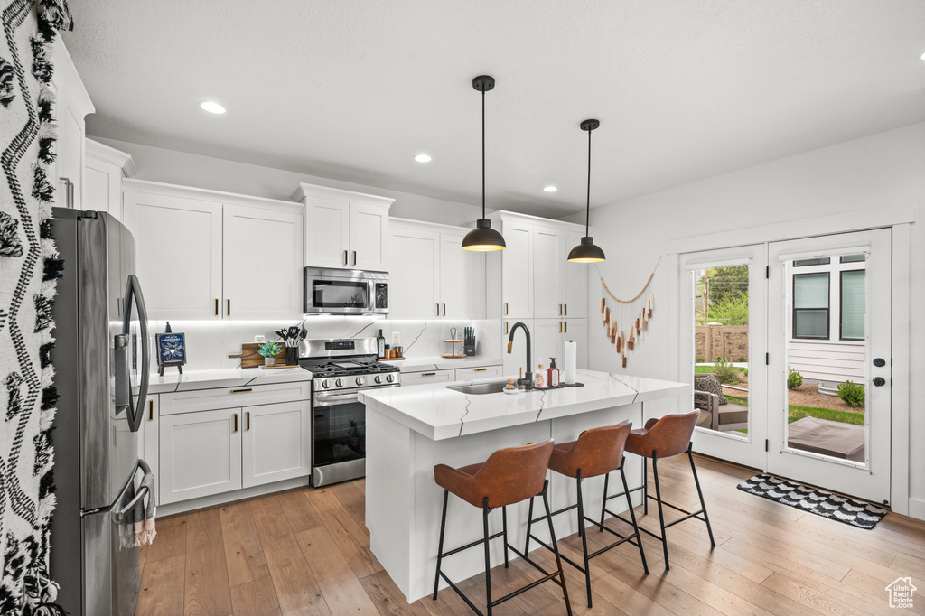 Kitchen featuring stainless steel appliances, a kitchen island with sink, light hardwood / wood-style floors, and white cabinetry